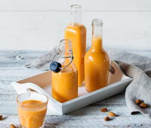 Apfel-Karotten-Saft mit Mandeln in Flaschen und Gläsern.