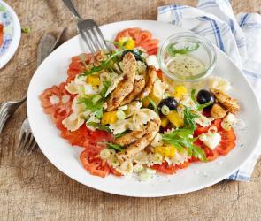 Bunter Nudelsalat mit gebratenen Hähnchenstreifen auf einem Teller.