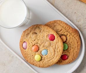 Cookies mit bunten Schokolinsen auf zwei Teller mit einem Glas Milch.