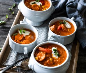 Deftiges Wurstgulasch in vier Suppenschalen auf einem Tablett.