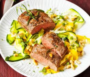 Gebratene Lammlachs auf einem Zucchini-Salat auf einem Teller.
