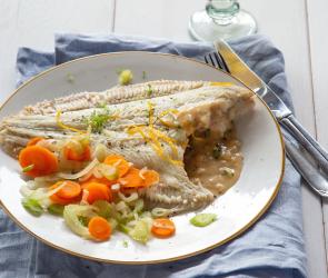 Teller mit Scholle und Gemüse, blaues Tuch, Besteck und Wasserglas