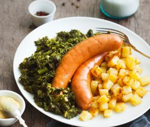 Grünkohl mit Wurst und Röstkartoffelwürfeln auf einem Teller angerichtet.