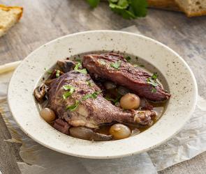 Hahn in Rotweinsoße (Coq au vin) auf einem Teller angerichtet.