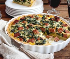 Quiche in der ein Stück fehlt, welches im Hintergrund auf einem Teller liegt. 