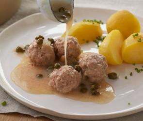 Königsberger Klopse mit Kartoffeln auf einem Teller, Soße wird dazugegeben.