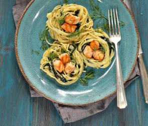 Lachs-Spaghettinester mit Gorgonzola und Spinat auf einem Teller.
