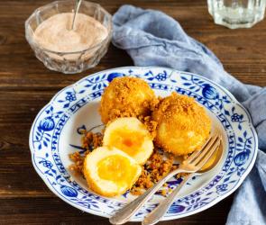 Marillenknödel auf Teller mit Besteck, Zimt-Zucker-Schälchen und Wasserglas mit Zitrone