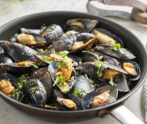 Muscheln in Weißwein (Moules marinières) in einer Schale auf einem Tisch.