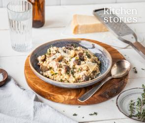 Risotto mit Salsiccia und Pilzen in einem Teller auf einem gedeckten Tisch.