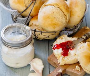 Mehrere Jogurtbrötchen in einem Körbchen und aufgeschnitten mit Marmelade bestrichen.