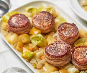 Schweinemedaillons auf Gemüse auf einer Servierplatte.