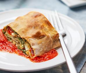 Ein Stück Spinatstrudel mit Tomaten und Schafskäse auf einem Teller.