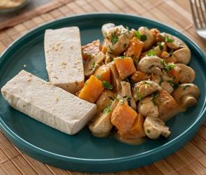 Tofu, gedämpft mit Kürbis und Champignons auf einem Teller.