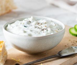 Tzatziki in Schale auf Brett mit Fladenbrot, Gurkenscheiben und weißem Tuch