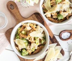 Vollkornpenne mit Hähnchen und Brokkoli in einem Teller auf einem Brett.