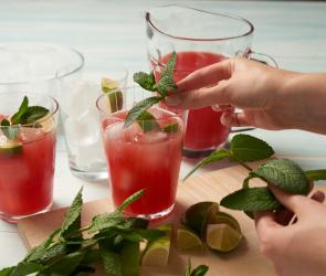 Wassermelonensaft in Gläsern und Karaffe, Limetten und Minze, Hand im Bild die Drinks dekoriert
