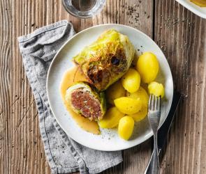 Wirsingrouladen mit Kartoffeln auf Teller und Auflaufform mit Rouladen