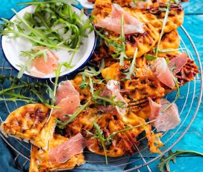 Schnelle Pizzawaffeln auf einem Gitter mit Schinken und Rucola.