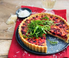 Quiche mit roter Bete und Rucola auf einem Servierteller.