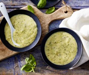 Grüner Zucchinibrei in Schälchen mit Löffel.