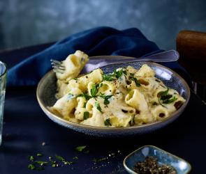 Pasta mit cremiger heller Sauce und Gemüse in einer Schale.