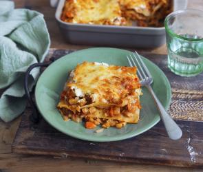 Lasagne in einer Auflaufform daneben ein Stück auf einem Teller.