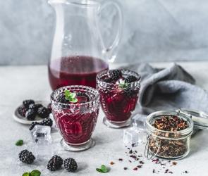 Eistee mit Brombeeren in Gläsern vor einer Karaffe.