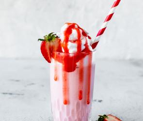 Erdbeer-Milchshake in einem Glas mit Sahne, Erdbeersauce, einer Erdbeere und einem Strohhalm.