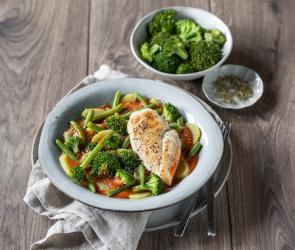 Hähnchen mit Gemüse und Tomatensauce in einer Schale angerichtet mit Brokkoli als Beilage.