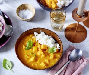 Einfaches Kürbis-Curry mit Reis in einer Schale auf einem gedeckten Tisch mit Kerzen.