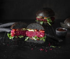 Black Bun Burger mit Rote Bete Patty halb aufgeschnitten auf einer dunkle Platte.