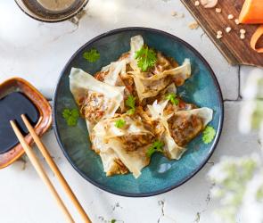 Gedämpfte Dumplings mit Gemüse auf einem blauen Teller.