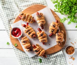 Hotdog-Stockbrot mit Röstzwiebeln auf einem Holzbrett.