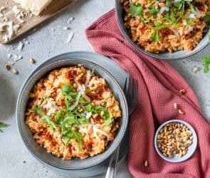 Risotto mit getrockneten Tomaten, Pinienkernen und Rucola in einer Schüssel.