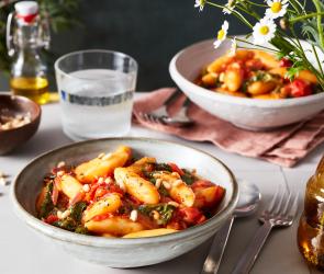 Schupfnudeln mit Spinat und Tomaten serviert auf einem gedeckten Tisch.