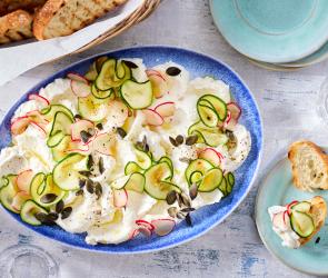Ricotta auf einem Teller mit Zucchini, Radieschen und Kürbiskernen.
