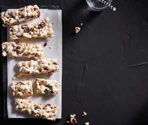 Müsliriegel mit Popcorn auf hellem Backpapier auf einem schwarzen Untergrund.