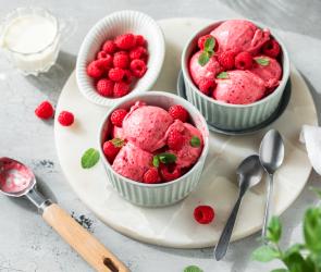 Himbeereis in Kugeln mit frischen Himbeeren und Minze dekoriert.