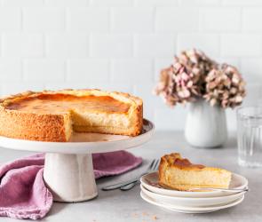 Veganer Käsekuchen auf einer Tortenplatte, angeschnitten.