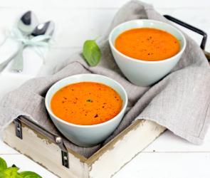 Cremige Tomatensuppe in hellen Schüsseln auf Tüchern.