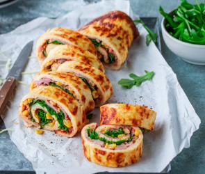 Low-Carb-Pizzarolle aufgeschnitten mit einem Messer auf einem Brett mit Papier angerichtet.