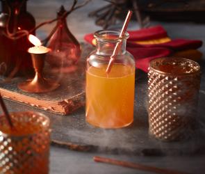 Zauberhafter Kürbissaft in einer Glasflasche mit Stohhalm, dahinter Halloween Deko.