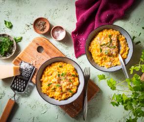 Kürbis Risotto in Schüsseln auf einem Holzbrett mit geriebenem Parmesan.