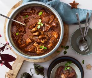 Wildgulasch in einer Schüssel mit frischen Kräutern.