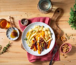 Pastinaken Püree getoppt mit Wurzelgemüse auf einem Teller auf einem gedeckten Tisch mit Honig.