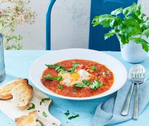 Shakshuka in einem hellen Teller mit Ei und Basilikum.