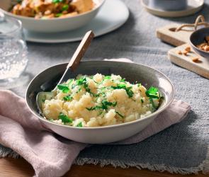 Blumenkohlreis in einer Schüssel mit Löffel und Kräutern garniert.