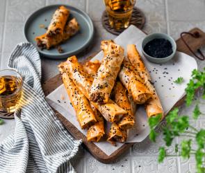 Börek mit Hackfleischfüllung knusprige Teigröllchen auf einem Brett.