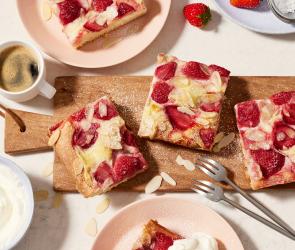 Erdbeerkuchen vom Blech in Stücke geschnitten auf einem Brett.